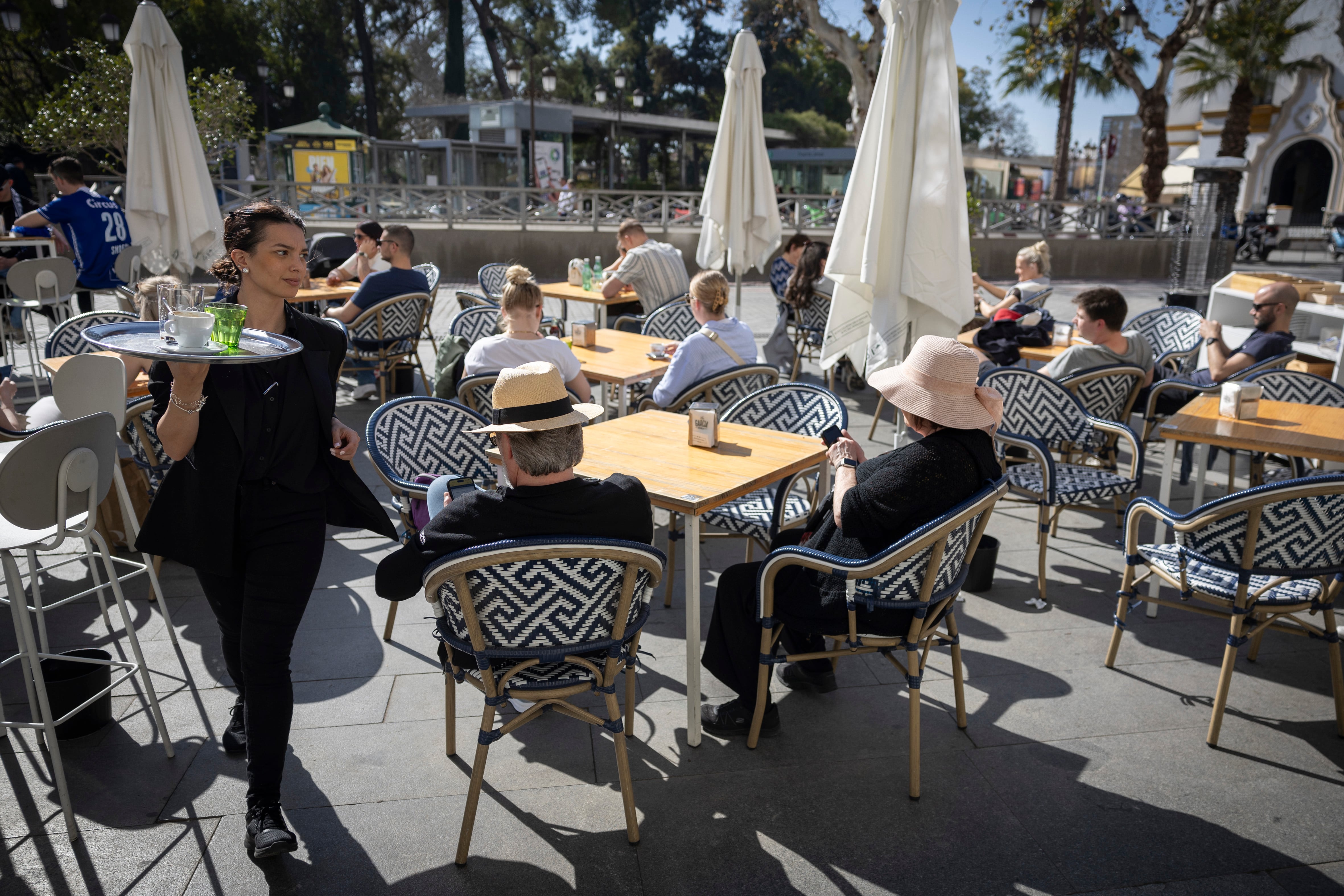 Una camarera atiende una terraza con turistas en Sevilla. 