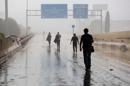 Varias personas transitan por la V-31 cerrada al tráfico a causa de las lluvias torrenciales de las últimas horas.