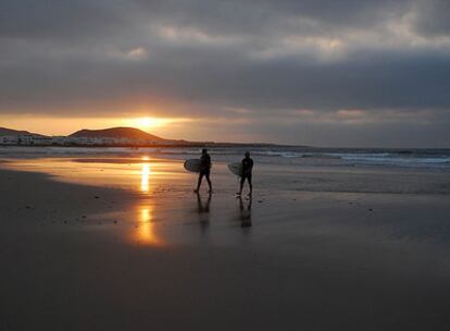 Dos surfistas salen del mar con sus tablas mientras se pone el sol en la playa de Famara.