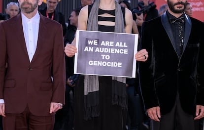 Invitados posan en la alfombra roja con un cartel que dice “We are all an audience to genocide” (“Todos somos público de un genocidio”) en referencia a la situación en Gaza, a su llegada al estreno de 'The Smashing Machine' durante la 82ª edición del Festival Internacional de Cine de Venecia, el 1 de septiembre de 2025.