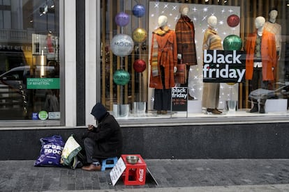 Un mendigo delante de un escaparate anunciando el Black Friday en la Gran Vía madrileña. La ropa, el calzado y los complementos se convirtieron durante el año pasado en la categoría que más ventas generó durante este evento; y no es para menos, ya que estos productos alcanzaron un descuento medio del 33%.