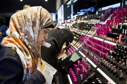 Dos mujeres en una tienda de cosmética. Una se levanta el velo islámico que le cubre el rostro para poder pintarse los labios mientras la otra habla por teléfono.