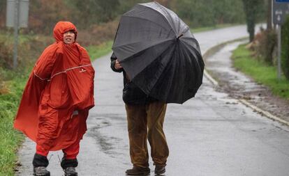 Una pareja se cubre de la lluvia y del viento en el paso del Camino de Santiago por Palas de Rei (Lugo).
