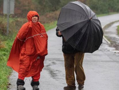Una pareja se cubre de la lluvia y del viento en el paso del Camino de Santiago por Palas de Rei (Lugo).