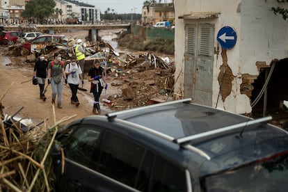 Un grupo de voluntarias caminan por la calle junto a un barranco en Paiporta.

