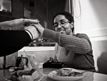 Si en una cafetería Gennet pierde el contacto con Alessandra se pone nerviosa. Estira el cuello como si la buscara. Se desubica. En la imagen, se están dando las gracias en lengua de signos apoyada, se escriben sobre la mano. Gennet lleva gafas para proteger sus ojos del polvo, ya que es propensa a coger infecciones. De niña, cuando llegó a España, su madre la llevó a varios médicos para que encontraran una solución a su enfermedad. No se podía. Como en la imagen, Gennet es sonriente, con una risa cantarina y contagiosa, que irrumpe en el momento más inesperado y que transmite optimismo.