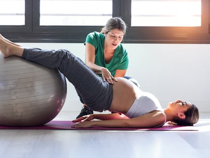 A pregnant woman does Pilates exercises with the help of a physical therapist.