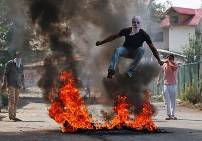 Un hombre con la cara cubierta con un pasamontañas salta sobre unos escombros en llamas durante una protesta en la Cachemira india.