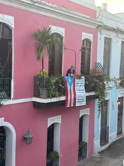 La escritora Magali García Ramis asomada a su balcón, con una bandera de Puerto Rico y una frase de Bad Bunny, durante las tradicionales fiestas de la calle de San Sebastián, en San Juan.