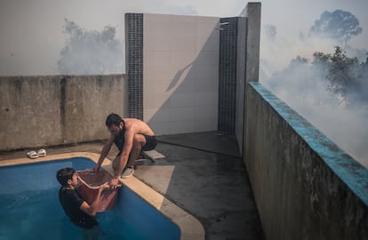 Portugal se enfrenta a una oleada de incendios que han afectado ya a 6.400 hectáreas. En la imagen, dos vecinos de Caneças, a las afueras de Lisboa, sacan agua de una piscina para intentar sofocar el fuego que amenaza sus viviendas, este pasado domingo.