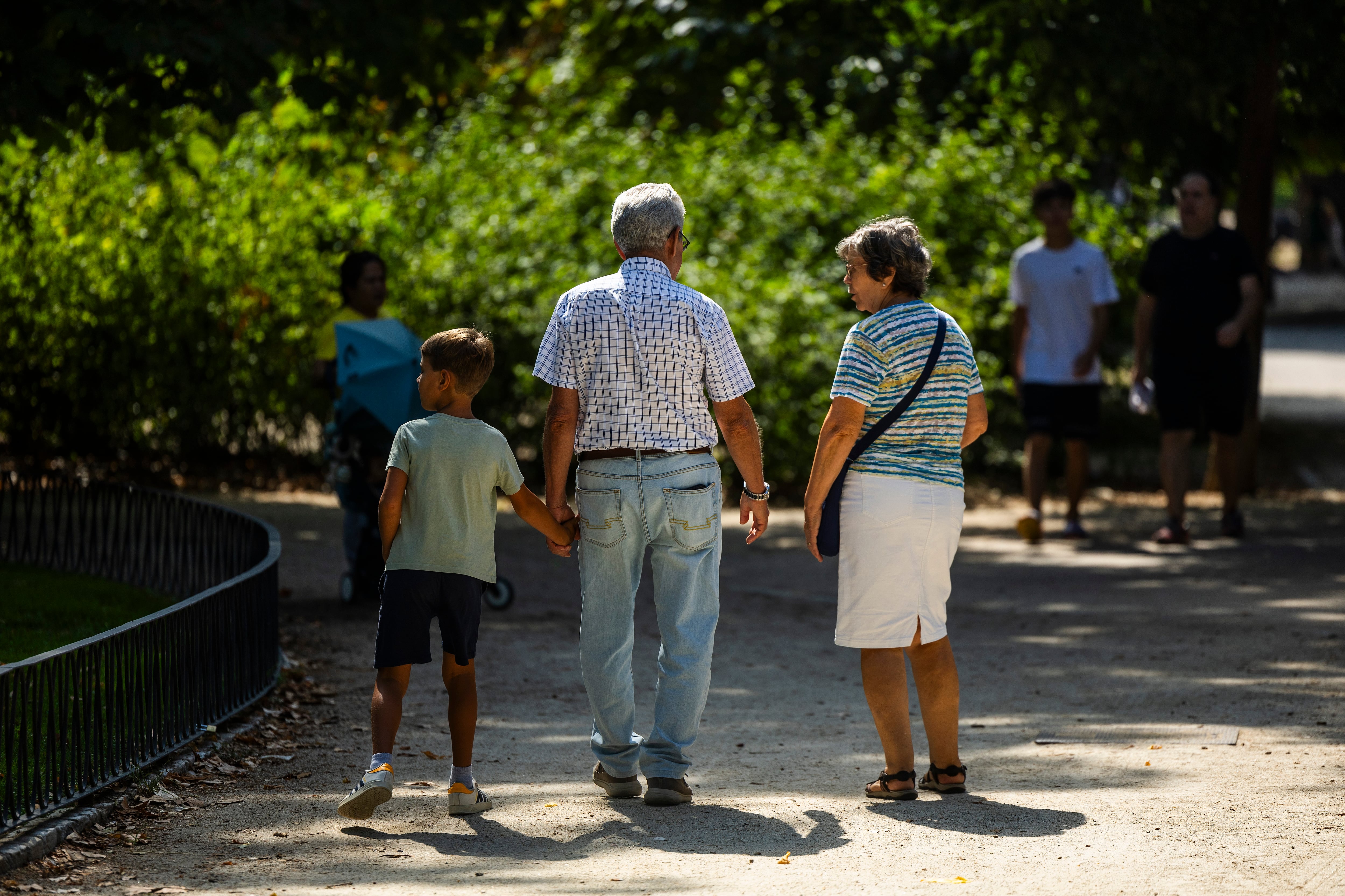 Dos personas mayores con un niño en el parque del Retiro de Madrid.
