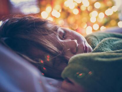 Una niña duerme junto a un árbol de Navidad.