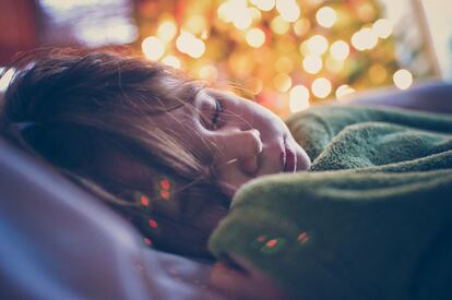 Una niña duerme junto a un árbol de Navidad.