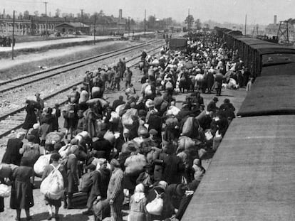 Chegada de deportados a Auschwitz. Ao fundo, as chaminés dos fornos crematórios.