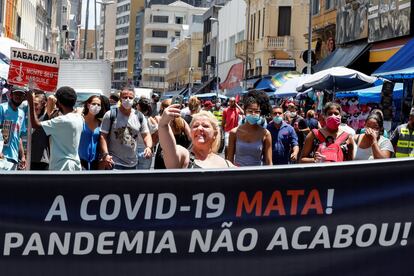 Uma mulher sem máscara, no centro de São Paulo, tira uma selfie atrás de uma faixa que diz: "A Covid-19 mata. A Pandemia não acabou".