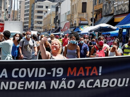 Uma mulher sem máscara, no centro de São Paulo, tira uma selfie atrás de uma faixa que diz: "A Covid-19 mata. A Pandemia não acabou".