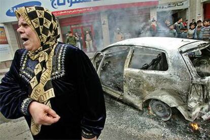 Una mujer camina junto a un coche incendiado durante choques entre milicias palestinas en Nablús.