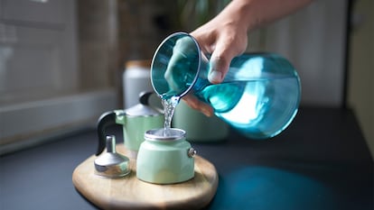 Una mano echando la pastilla diluida en agua en una cafetera.