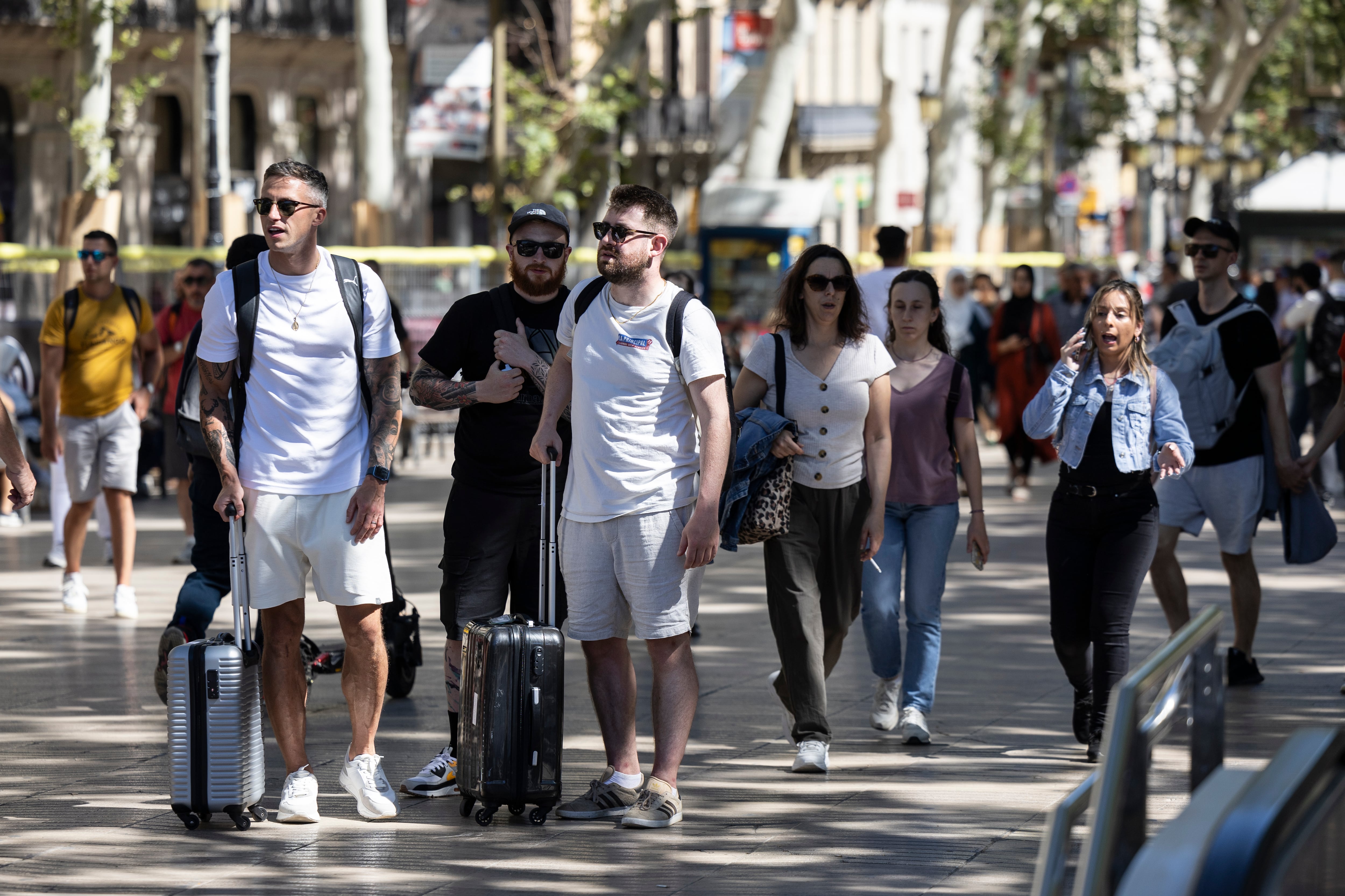 Varios turistas con maletas pasean por Las Ramblas de Barcelona.