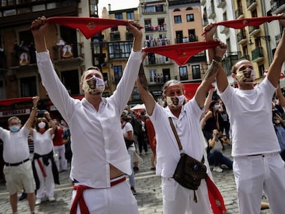 Varias personas, vestidas de blanco y rojo, alzan sus pañuelos al aire a la hora en la que tendría que haberse celebrado el chupinazo de los sanfermines de 2020.