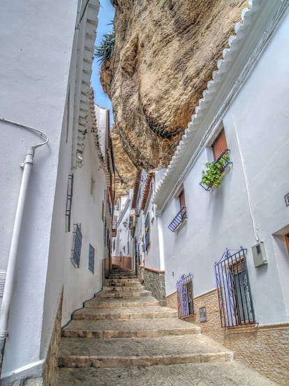 Setenil se esconde en el paisaje, pero no en forma de cuevas, como en otros muchos pueblos andaluces, sino que las casas se agazapan bajo el saliente de una roca gigantesca, como si estuviesen sujetándola, apuntalándola. Atravesar sus calles da cierto miedo por la sensación de que en cualquier momento pueda haber un desprendimiento. Esta original morfología del terreno confiere a Setenil de las Bodegas una personalidad única y diferente al resto de <a href="https://elviajero.elpais.com/elviajero/2016/11/10/actualidad/1478771717_506401.html" target="_blank">los llamados Pueblos Blancos de la sierra de Cádiz</a>. Y ya no son solo las casas encaladas bajo la roca, sino que se han ido creando calles-cueva, miradores y rincones curiosísimos. Un escenario casi mágico, lleno de tajos y visiones inesperadas, donde incluso se celebran fiestas tan curiosas como la Semana Santa setenileña. Su origen medieval, almohade concretamente, se hace visible en el espacio de La Villa, en la Torre del homenaje de una gran fortaleza medieval que se conserva y en un aljibe subterráneo de la época. Hay restos mudéjares en la antigua casa consistorial y se puede seguir el legado histórico de Setenil ligado a la conquista cristiana de 1484 en la llamada ruta de los Reyes Católicos, de la que forma parte. Y para quien prefiera naturaleza abierta, en los alrededores hay una amplia oferta de senderos y rutas.