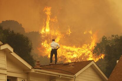 Un hombre sobre el tejado de una casa observa como avanzan las llamas del incendio, cerca de Camarillo, California. El fuego ha arrasado ms de 11.000 hectreas al norte de Los ?ngeles.