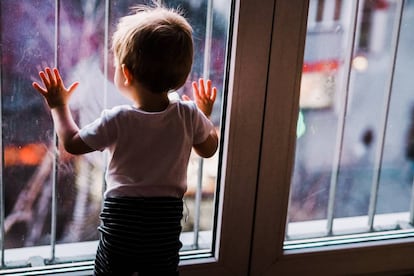 Un niño mira por la ventana de su cuarto la calle. 