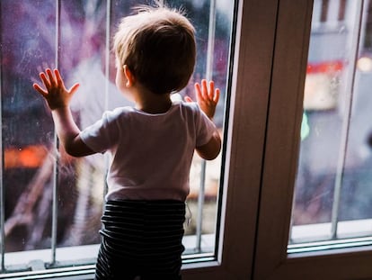 Un niño mira por la ventana de su cuarto la calle. 