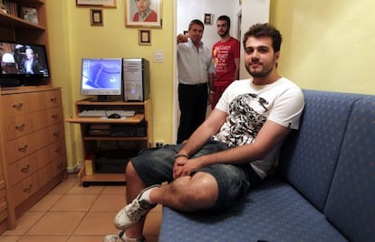 David Sánchez, 27 years old sits in his room with his brother Víctor (22), behind, and their father Francisco.