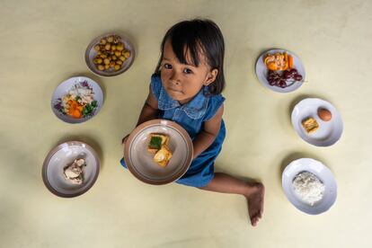 “Las conclusiones del informe son claras: millones de niños pequeños reciben una alimentación que los predispone al fracaso justo cuando los riesgos son más elevados”, ha afirmado la directora ejecutiva de Unicef, Henrietta Fore. En la foto, Gelsi, indonesia de tres años, sostiene un plato de tofu en su casa en la localidad rural de Paseban, en la isla de Java. Los otros alimentos adicionales que aparecen en la imagen son: pollo cocido, huevo cocido, sopa de verduras, arroz, naranja, uvas y longan u ojo de dragón chino, que es una fruta típica de esta región.