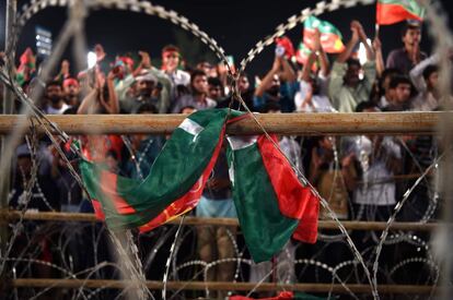 Una bandera del partido político Pakistan Tehreek-e-Insaf (PTI) se ve en primer plano mientras partidarios de la estrella de cricket paquistaní convertida en político y jefe del partido asiste a una reunión de campaña antes de las elecciones generales en Lahore, el 23 de julio de 2018.