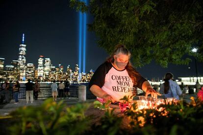 Un grupo de gente enciende velas en recuerdo de las víctimas del 11-S. Al fondo, un tributo de luz instalado en el One World Trace Center por el vigésimo aniversario de los atentados