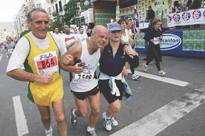Dos  corredores veteranos ayudan a un tercero con problemas a que cruce la meta situada en  el Boulevard de San Sebastián.