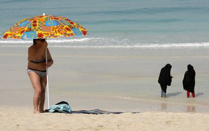 Una turista coloca una sombrilla mientras dos mujeres se mojan los pies en una playa de Dubái.