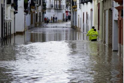 Dos personas recorren una de las calles de la localidad sevillana de Écija, inundada por las fuertes lluvias.