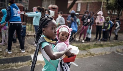 Una niña con un bebé en brazos recoge la comida que una asociación reparte en Johannesburgo (Sudáfrica) para las familias más pobres.