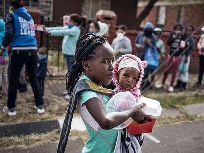 Una niña con un bebé en brazos recoge la comida que una asociación reparte en Johannesburgo (Sudáfrica) para las familias más pobres. 