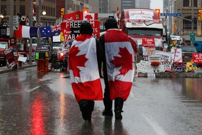 Manifestantes caminan con banderas canadienses, mientras los camioneros y sus simpatizantes continúan protestando contra las medidas de prevención ante la pandemia de covid, en Ottawa, Canadá. El centro de la capital canadiense permanece en tensión después de que la Policía advirtiera el miércoles de que el bloqueo con camiones de los antivacunas es "ilegal" y les exigiera que levantasen de inmediato su protesta.