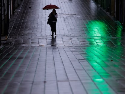 Una mujer camina con un paraguas la mañana de este viernes por una de las calles del centro de la ciudad coruñesa de Ferrol.