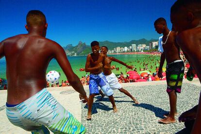 En la playa del Arpoador, en la zona sur de Río de Janeiro, cinco chicos juegan a la pelota en la acera. Al fondo, la playa y el monte Dois Irmãos.