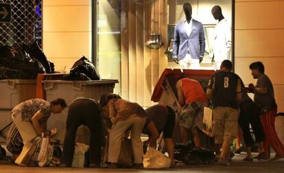 Un grupo de personas buscan en bolsas de basura alimentos a las puertas de un centro comercial  en la calle Alberto Aguilera, en Madrid