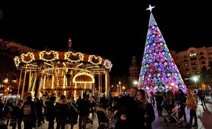 Una pareja se toma una fotografía ante el árbol de Navidad y el carrusel en la plaza del Ayuntamiento de Valencia.
