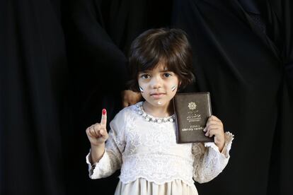 Una niña muestra su dedo manchado en tinta y el pasaporte de su madre después de votar.