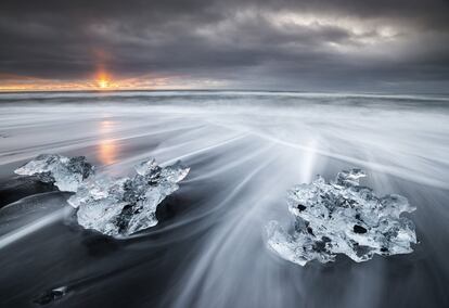 El sol asoma regalando la única nota de color a una mañana en la que trozos de hielo glaciar están varados en una playa de arena volcánica en el sur de Islandia.