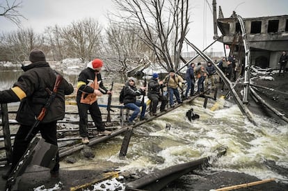 Miembros de una unidad de defensa civil ucrania reparten rifles de asalto, haciendo una cadena humana, en un puente volado del frente norte de Kiev.