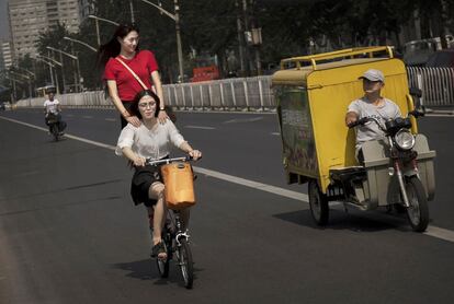 Condutor de um triciclo de carga observa duas moças que trafegam em uma bicicleta por uma rua de Pequim (China).