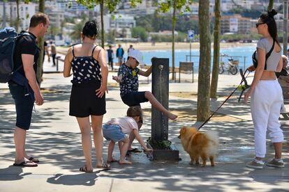 Una familia francesa de Toulouse, que pasa cuatro días en Roses (Girona), se refresca en una fuente del paseo marítimo, en mayo de 2022. 