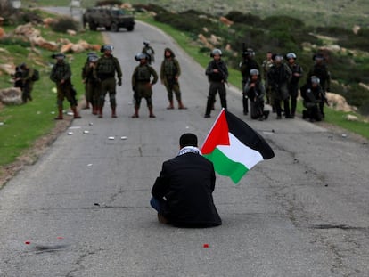 Un manifestante con una bandera palestina se sienta frente a las fuerzas israelíes durante una protesta contra los asentamientos israelíes en febrero.