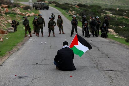 Un manifestante con una bandera palestina se sienta frente a las fuerzas israelíes durante una protesta contra los asentamientos israelíes en febrero.