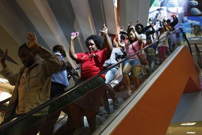 Un grupo de personas abandona el centro comercial con los brazos en alto.